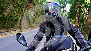 Motorcycle ridding from front angle at twisty mountain road with lush green forests