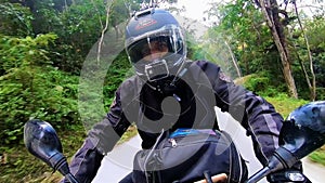 Motorcycle ridding from front angle at twisty mountain road with lush green forests