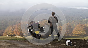 Motorcycle and standing rider in an autumn valley.