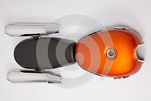 Motorcycle tank orange with black seat and chrome silver mufflers exhaust part motorbike in flat lay top view