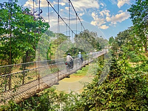 Motorcycles crossing a flimsy suspension bridge in Cambodia.