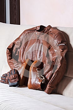 Motorcycling Outfit Concepts. Set of Tanned Leather Stylish Motorcyclist Equipment Outfit Placed Together On Couch Indoors