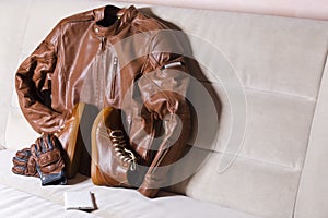 Motorcycling Outfit Concepts. Set of Tanned Leather Stylish Motorcyclist Equipment Outfit Placed Together On Couch Indoors