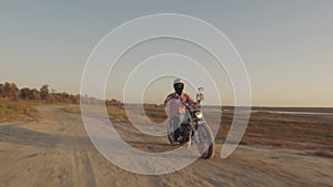 Motorcyclist driving his motorbike on the dirt road during sunset 4k shot