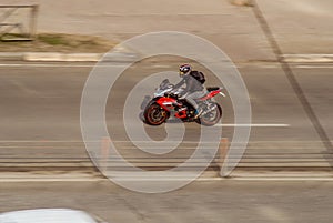 Motorcyclist driving on red motorcycle on the city street. Biker on red sport bike riding on empty street with motion blur effect