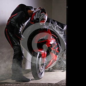 Motorcyclist in full gear and helmet removes the cover from the red sports motorcycle. Dust cover on the motorcycle