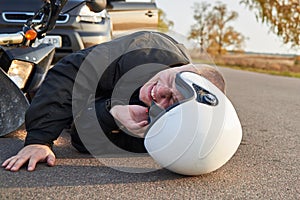 A motorcyclist lies on the asphalt near a motorcycle and car