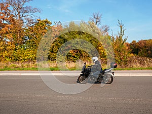 Motorcyclist in motion. Woman biker on a black motorcycle in traffic on a rural autumn road.