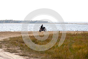 Motorcyclist quickly rides along sandy coastline along beach near water lake