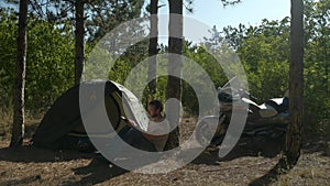 Motorcyclist sitting near tent in woods and reading a book at vacation near camp