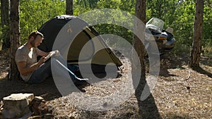 Motorcyclist sitting near tent in woods and writing a book at vacation near camp