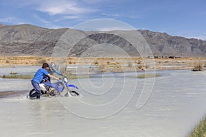 A motorcyclist takes a motorcycle through a white mountain river, his friend helps him. Mongolia, Altai