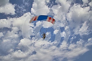 Motorized hang glider flies in a blue cloudy sky