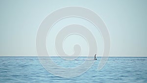 A motorized surfboard with a rider moving on a calm sea. The silhouette of a man on a water scooter glides through the