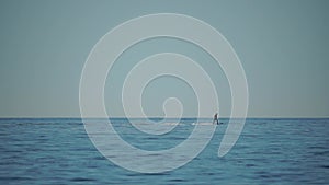 A motorized surfboard with a rider moving on a calm sea. The silhouette of a man on a water scooter glides through the