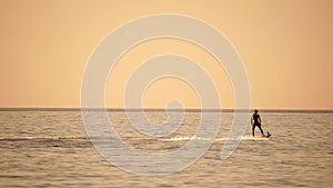 A motorized surfboard with a rider moving on a calm sea. The silhouette of a man on a water scooter glides through the