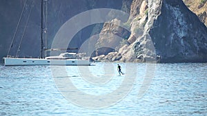 A motorized surfboard with a rider moving on a calm sea. The silhouette of a man on a water scooter glides through the