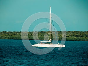 Motorsailer at anchor on steep green coast hill background. Luxury pleasure craft yacht with lowered sails on calm sea water.