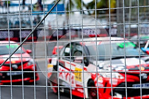 Motorsport car racing on asphalt road. View from the fence mesh netting on blurred car on racetrack background. Super racing car