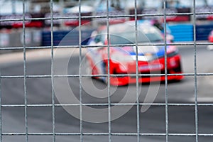 Motorsport car racing on asphalt road. View from the fence mesh netting on blurred car on racetrack background. Super racing car