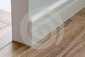 Moulding in the corner. Light matte wall with tiles immitating hardwood flooring