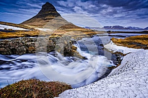 Mount Kirkjufell towers over rushing waterfalls in Iceland.