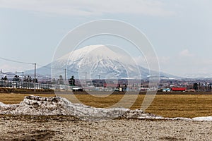 Mount Yotei inactive stratovolcano with village on the foot hill and yellow grass on the ground with pile of snow on foreground