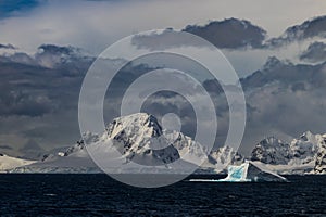 Mountain, Antarctic Peninsula. Blue iceberg in foreground; clouds in background.