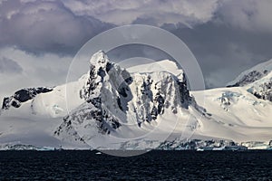 Mountain, Antarctic Peninsula. Snow, rocks; Clouds in background.