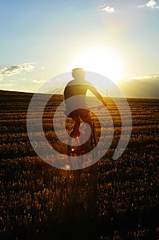 Mountain bike rider riding through beautiful straw field against burning summer sun at sunset