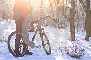 Mountain Biker with his Bike on the Snowy Trail in the Beautiful Winter Forest Lit by Sun