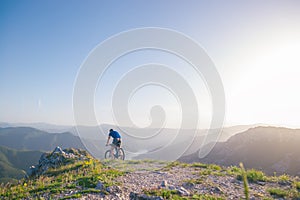 Mountain biker holding his bike on a rough cliff terrain on a sunset