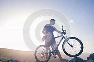 Mountain biker holding his bike on a rough cliff terrain on a sunset