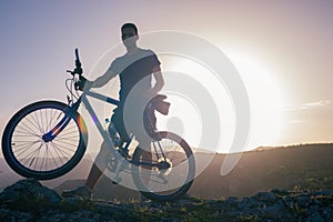 Mountain biker holding his bike on a rough cliff terrain on a sunset