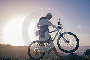 Mountain biker holding his bike on a rough cliff terrain on a sunset