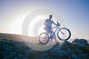 Mountain biker holding his bike on a rough cliff terrain on a sunset