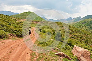 Mountain biker riding the bike in road among green meadows