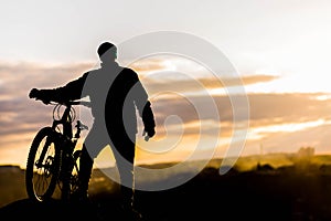 Mountain biker standing on top of a mountain with a bicycle, a beautiful sunset. Silhouette of a cyclist