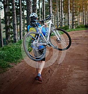 Mountain bikers are a tough lot. a male cyclist walking along a trail carrying his mountain bike.