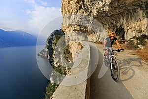 Mountain biking at sunrise woman over Lake Garda on path Sentiero della Ponale, Riva del Garda, Italy