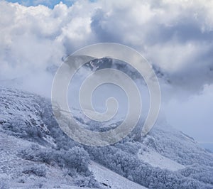 Mountain chain cowered by a snow in a mist and dense clouds