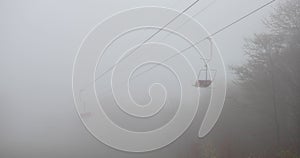 Mountain chair lift working in the fog. Working cable car with over the forest in the mountains in summer in fog.