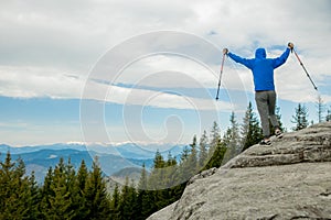 A mountain climber is high in the mountains against the sky, celebrating the victory, raising his hands up