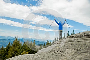 A mountain climber is high in the mountains against the sky, celebrating the victory, raising his hands up