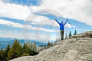 A mountain climber is high in the mountains against the sky, celebrating the victory, raising his hands up