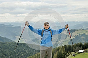 A mountain climber is high in the mountains against the sky, celebrating the victory, raising his hands up