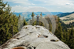 A mountain climber is high in the mountains against the sky, celebrating the victory, raising his hands up.