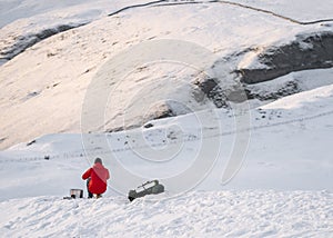Mountain climber in red coat on white snow covered mountain hill taking break to keep warm eat and drink. Looking at hillside