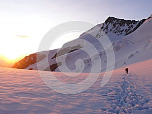 Mountain climber on a rope walking across a large glacier in the Swiss Alps just after sunrise