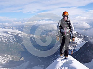 Mountain climber on a steep and narrow snow ridge leading to a high peak in the Swiss Alps